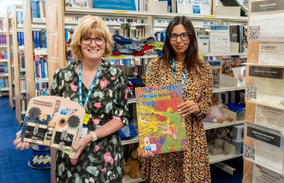 2 female colleagues smiling at camera, while holding patient support resources (a book and board with sensory activities)